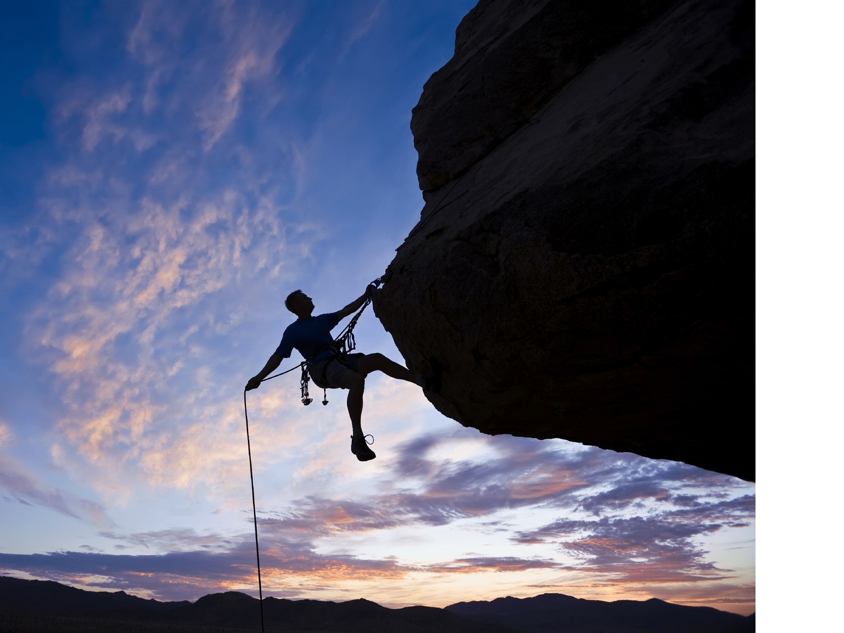 A rock climber is silhouetted against the evening sky as he rappels past an overhang in Joshua Tree National Park.