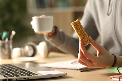 Photo of someone with a cereal bar in one hand and a cup in the other